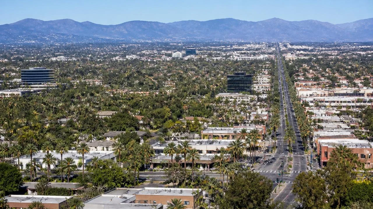 Aerial view of a Southern California boulevard lined with palm trees, with mountains in the distance